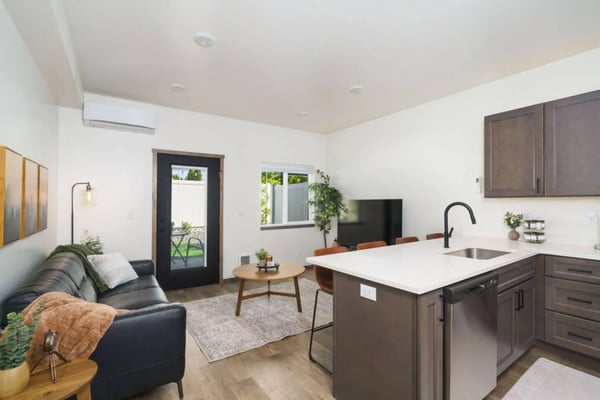 Open-plan living room and kitchen with dark leather sofa, white countertops, dark wood cabinets, and glass door to patio